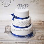 Klasyczny biały piętrowy tort weselny z pikowaną polewą i granatową wstążką