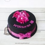 244BA Tort z czarną polewą, różowymi kwiatami z masy cukrowej, przewiązany lukrowaną kokardą
