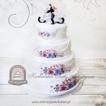 Weselny tort piętrowy z girlandą, zdobieniem kwiatowym oraz figurką Pary Młodej na motorze